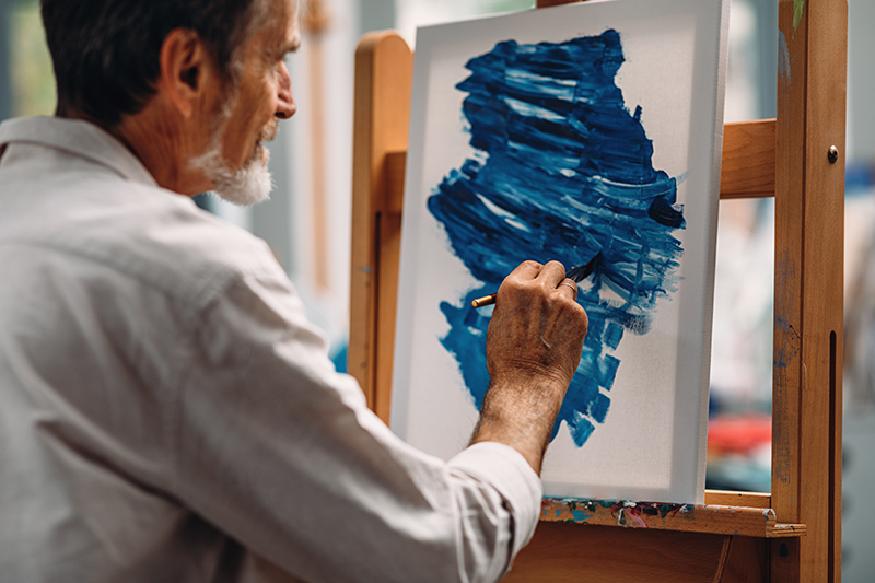 Aikuinen henkilö maalaa sinistä värikokeilua maalaustelineessä olevalle paperille.