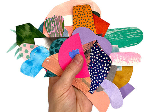 Käsi pitelee eri muotoihin leikattuja värikkäitä paperinpaloja.