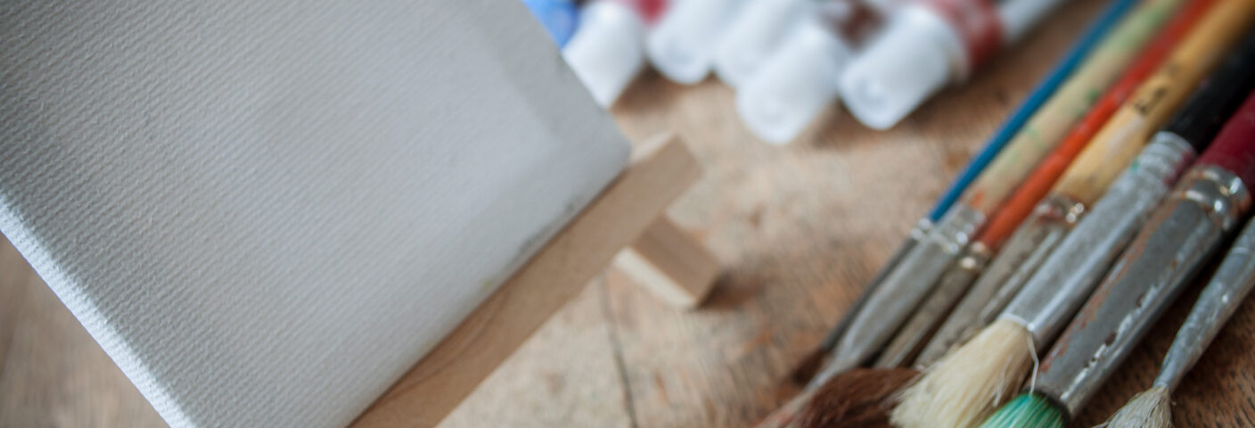 työpöydällä maalauspohja, akryylivärejä ja siveltimiä